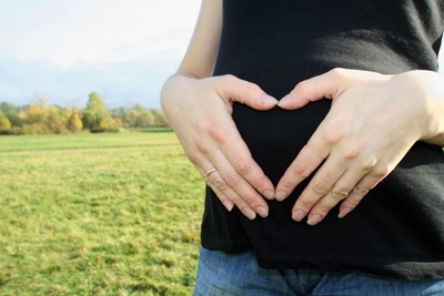 Pregnant women with hands over belly in a heart shape